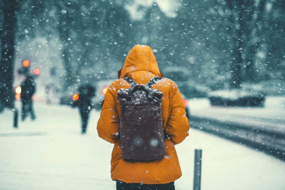 man in a coat wearing a backpack walking through the snow