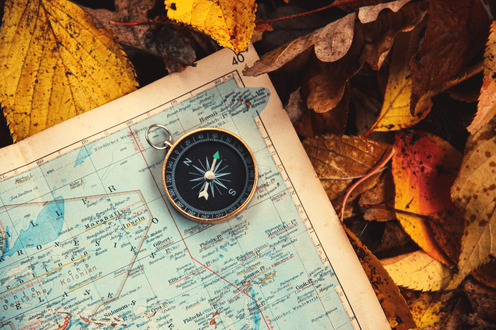 small compass resting on a map on the ground with fallen leaves