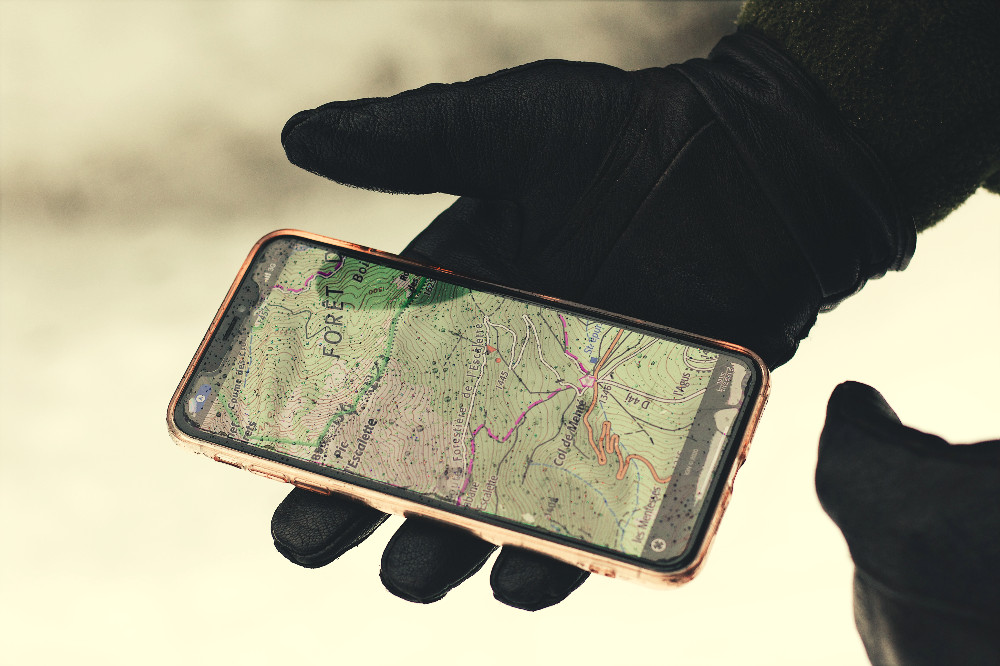 person wearing black gloves holding a cell phone with a map
