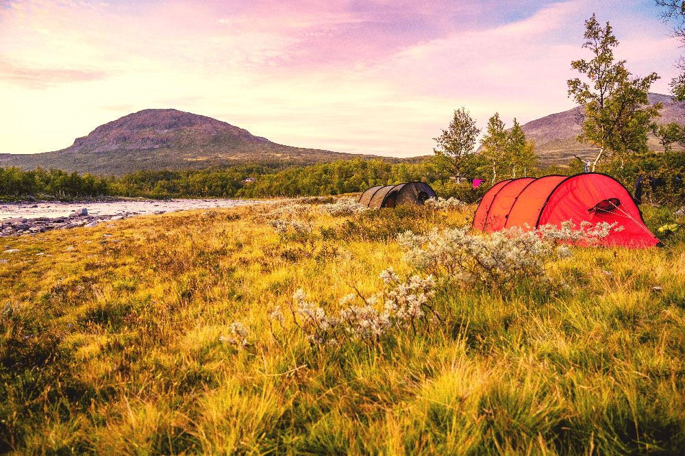 a red pop up tent on a grassy field next to a river
