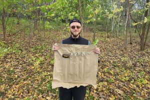 man holding a container of tent stakes and a mallet in the forest