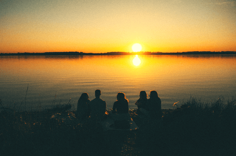 group of people around a lake at sunset