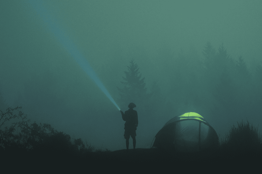 person next to a tent shining a light in bad weather