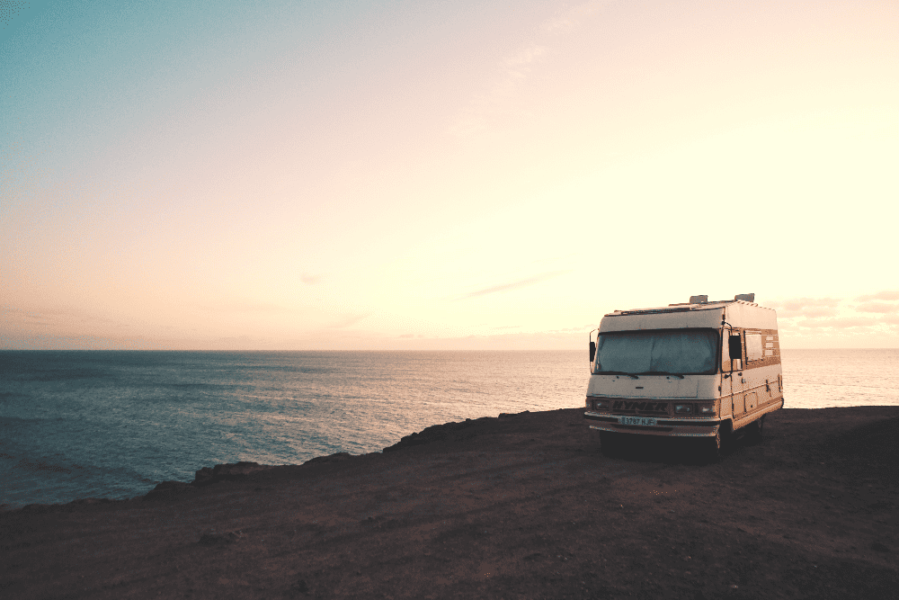 old rv set up on the coast next to an ocean at sunset