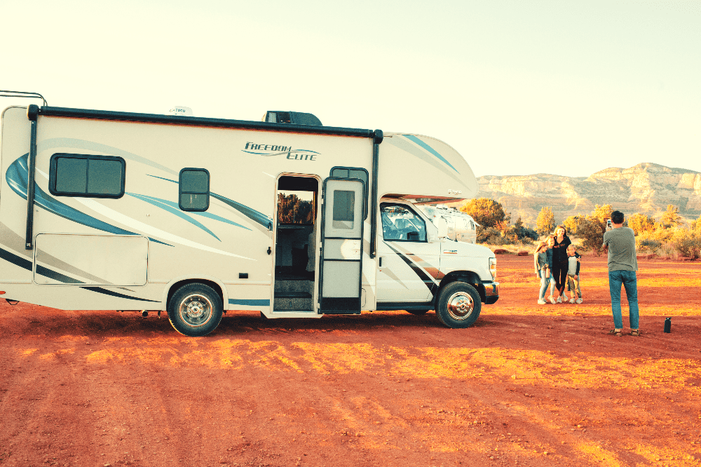 an rv parked on dirt with a family taking pictures