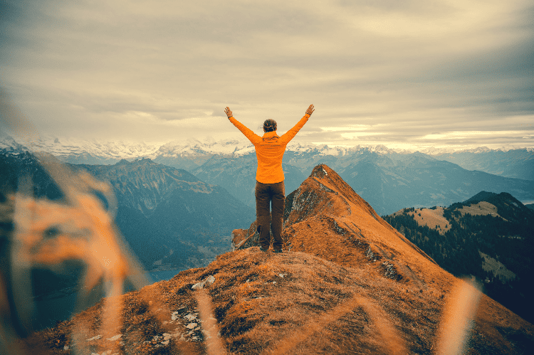 person with raised arms on top of a ridge