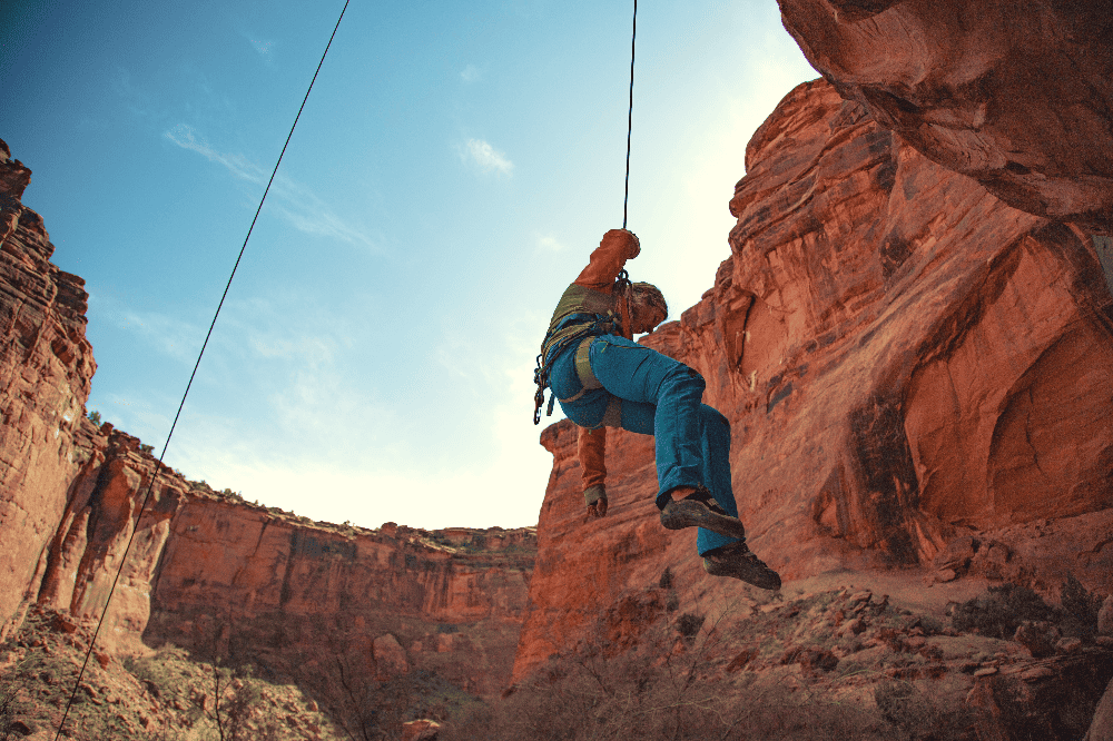 man being lowered from rock climbing in moab utah