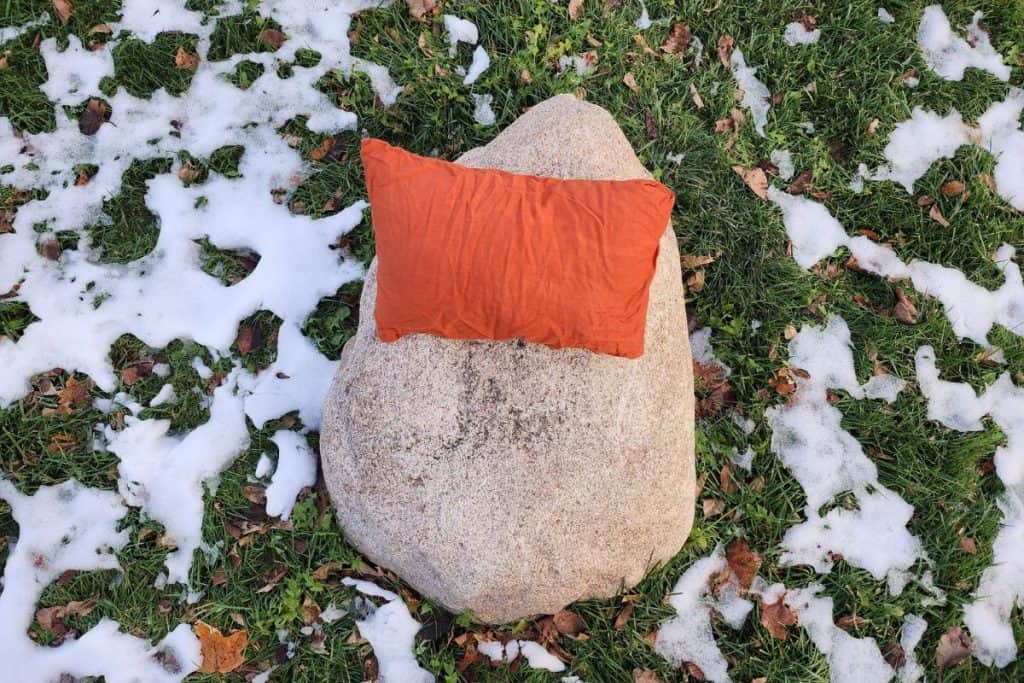 orange pillow on a rock with grass and snow