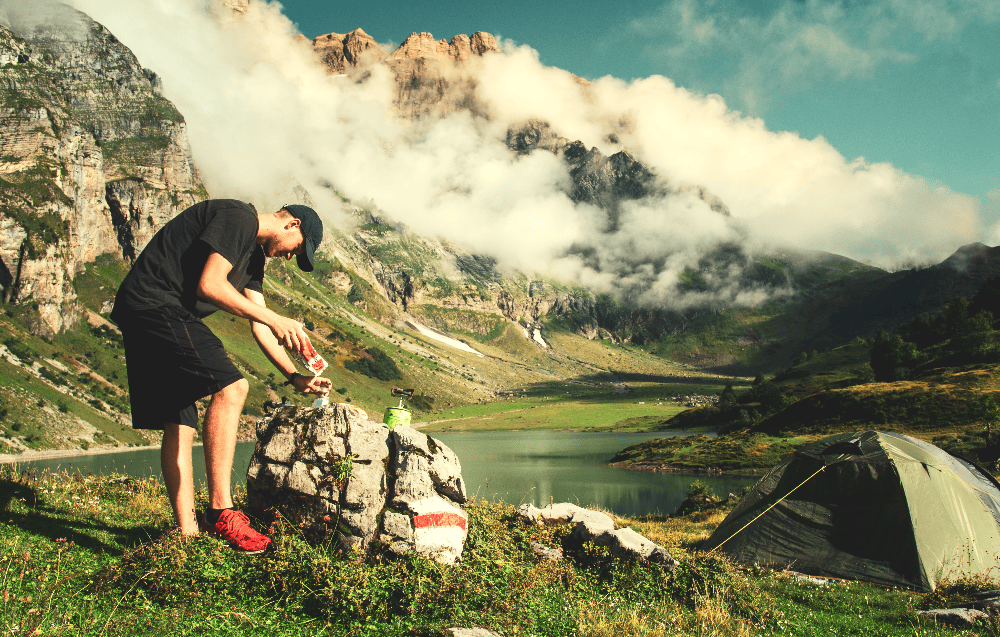 man making coffee while camping in mountains