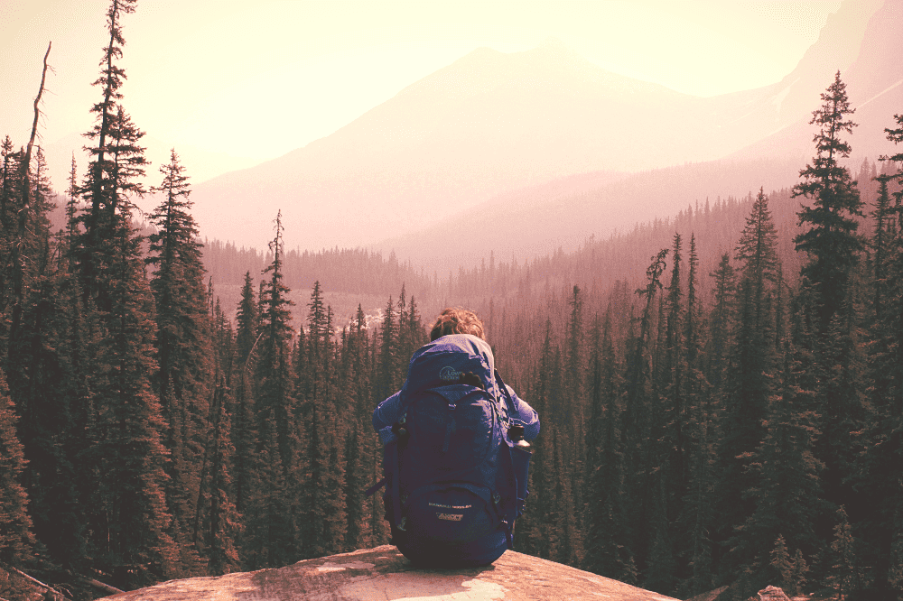 person sitting on a rock ledge with a backpack