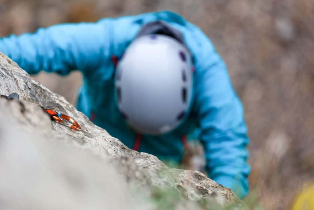 person climbing a rock wall with a blue jacket and white helmet