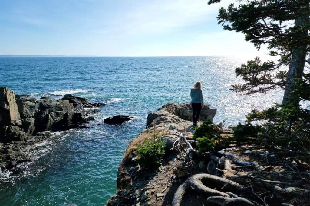 woman walking along a rocky trail by the ocean in maine