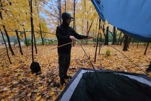 man in black jacket standing outside in the rain pitching a tent