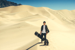 man standing with a snowboard on sand dunes