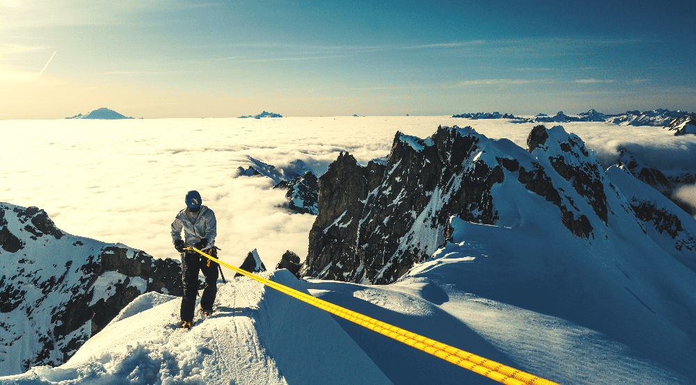 man rappelling down a snowy mountain