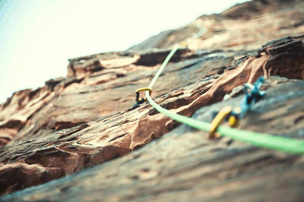 a green rope traveling through several quickdraws on a rock climbing route