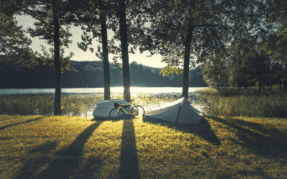 tent and bike set up next to trees and a lake