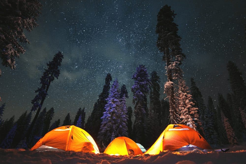 three tents with lanterns next to each other in a forest at night