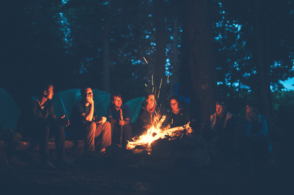 a group of people surrounding a campfire at nighttime