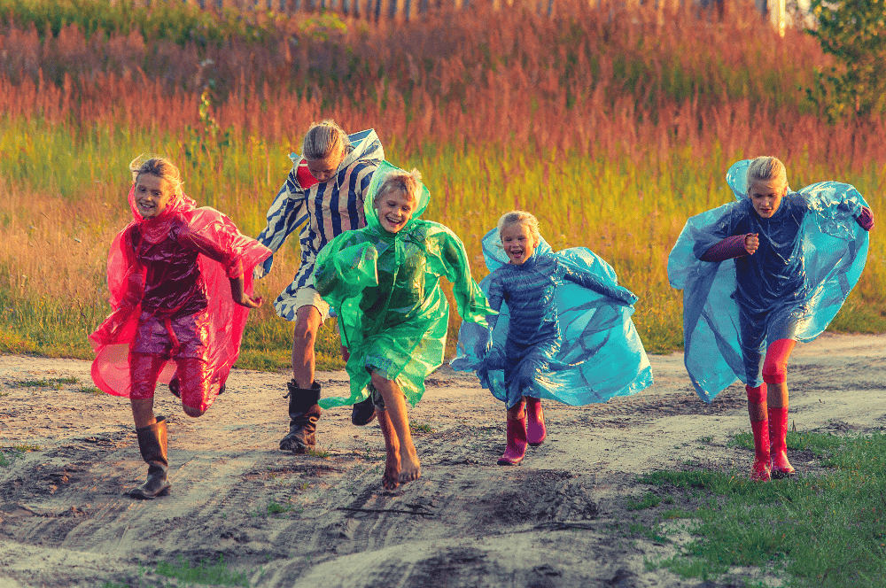 five russian kids running down a dirt road with ponchos on