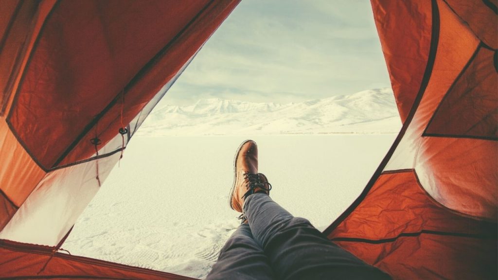 man laying in a tent with brown shoes surrounded by snow