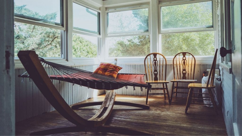 hammock on a hammock stand inside a house next to three chairs