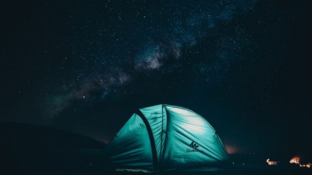 blue tent with a light in a forest at night under stars