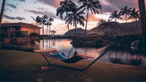 woman laying in a hammock on a hammock stand next to water during sunset
