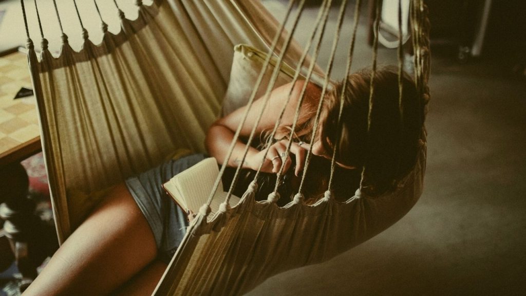 woman lying in a hammock inside while holding a notebook