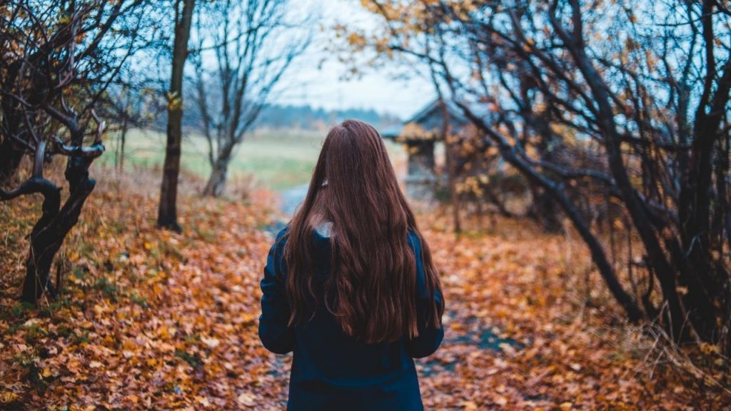 woman in a coat walking down a trail next to leaves on the ground