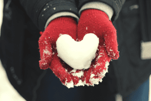 women wearing red gloves while holding a heart shaped piece of snow