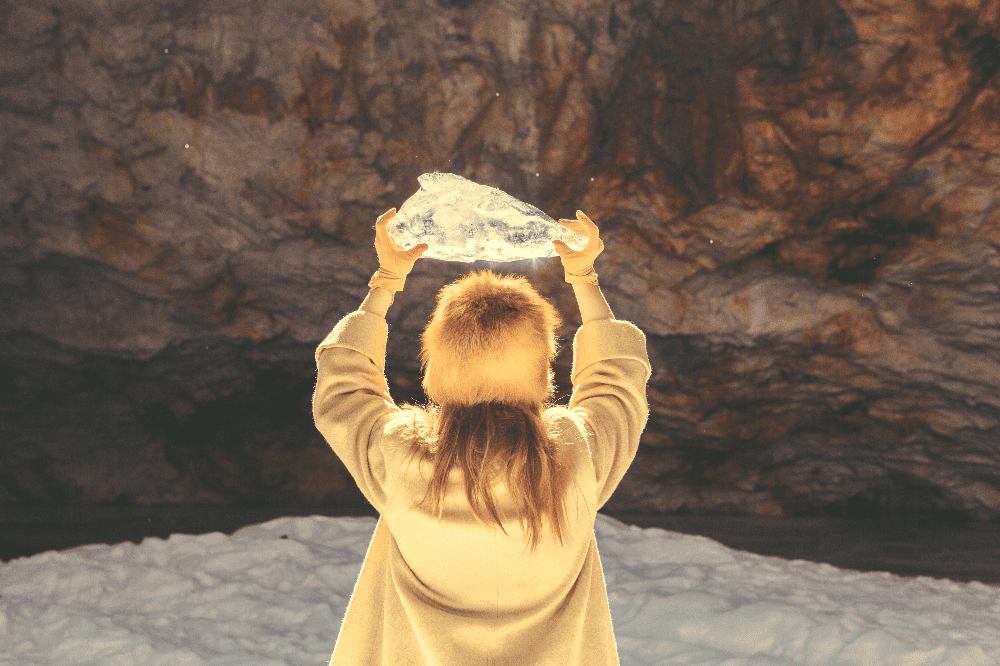 woman wearing a fuzzy hat and gloves holding a block of ice in the air