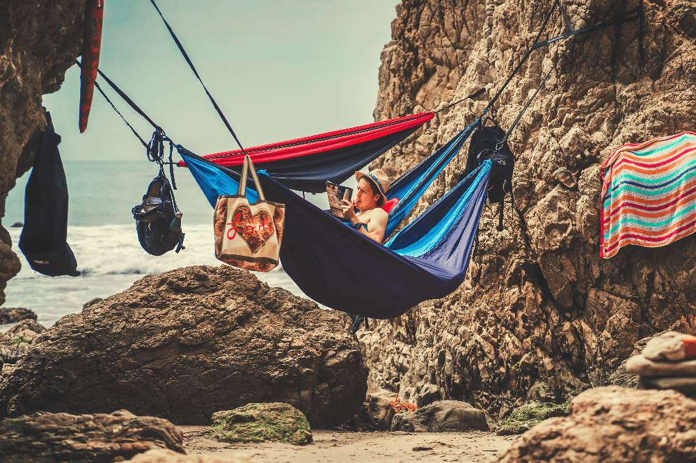 man sitting in a hammock with two other hammocks next to him on the beach in california