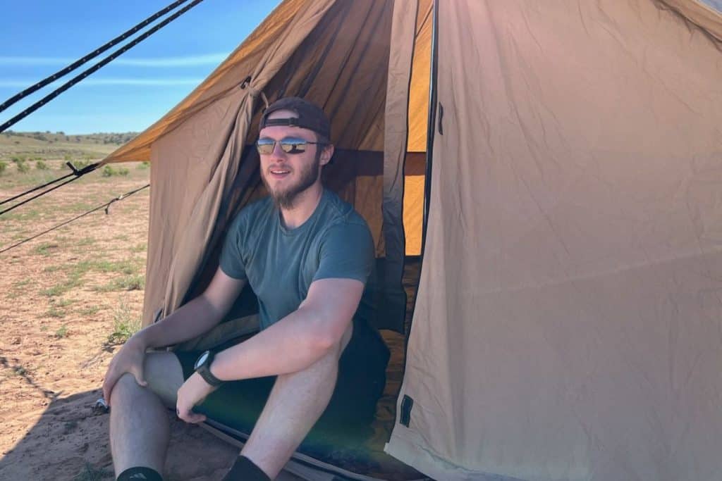 man in hat and sunglasses sitting in a canvas tent