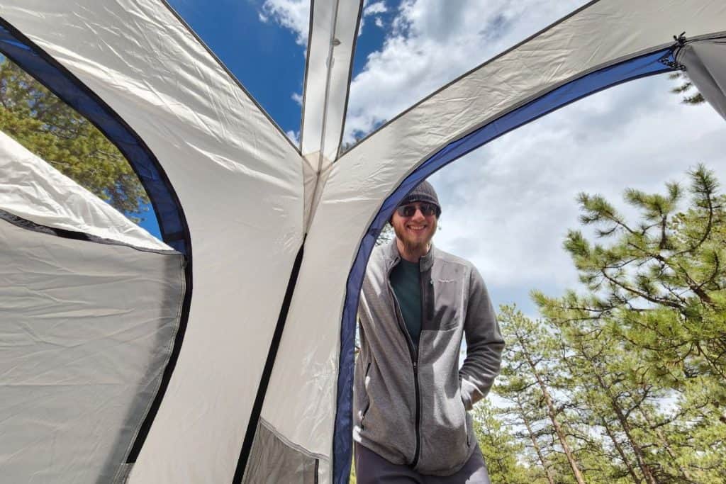man in hat and gray jacket standing at the entryway of a tent
