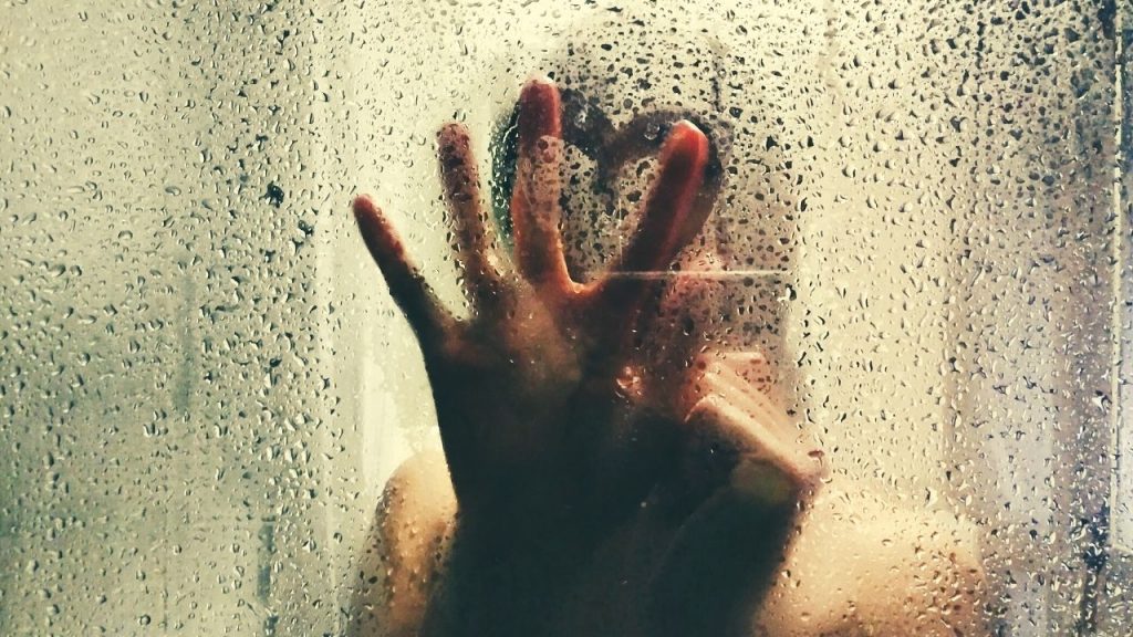 person standing in a shower with their hand pressed against the wall