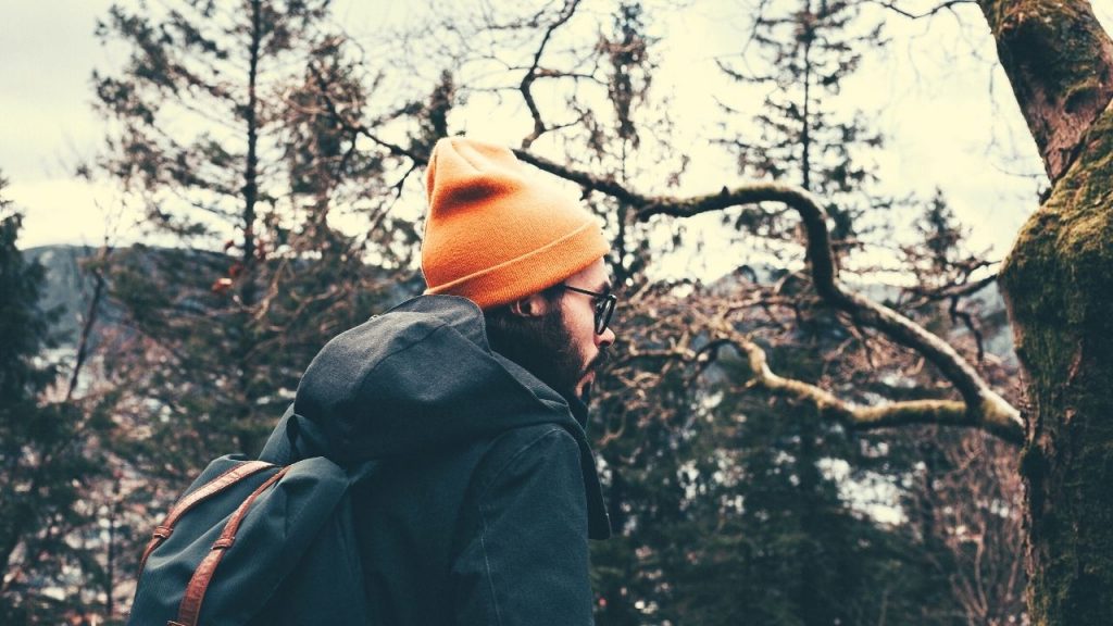 man wearing an orange hat and gray coat with backpack standing outside in the winter