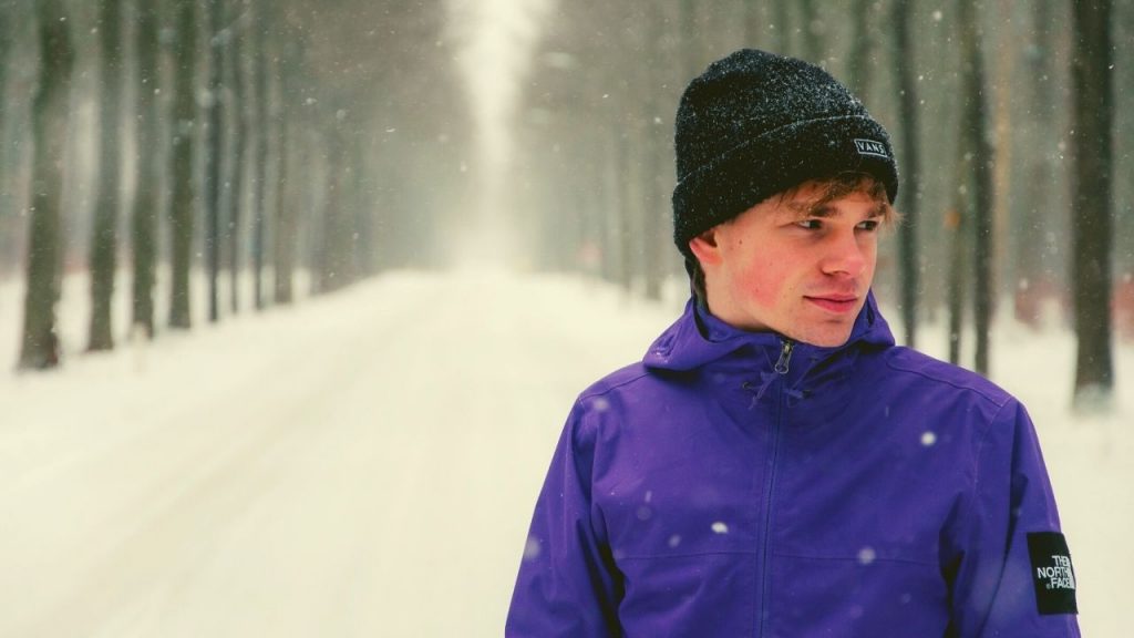 man in a purple jacket and gray hat standing outside in the snow