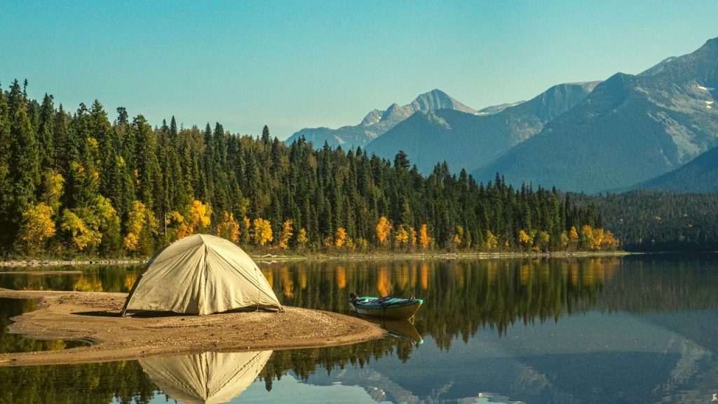 Tent on a sandy beach next to water and the mountains
