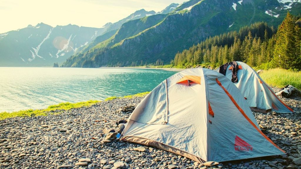 two tents on the beach next to water and the mountains