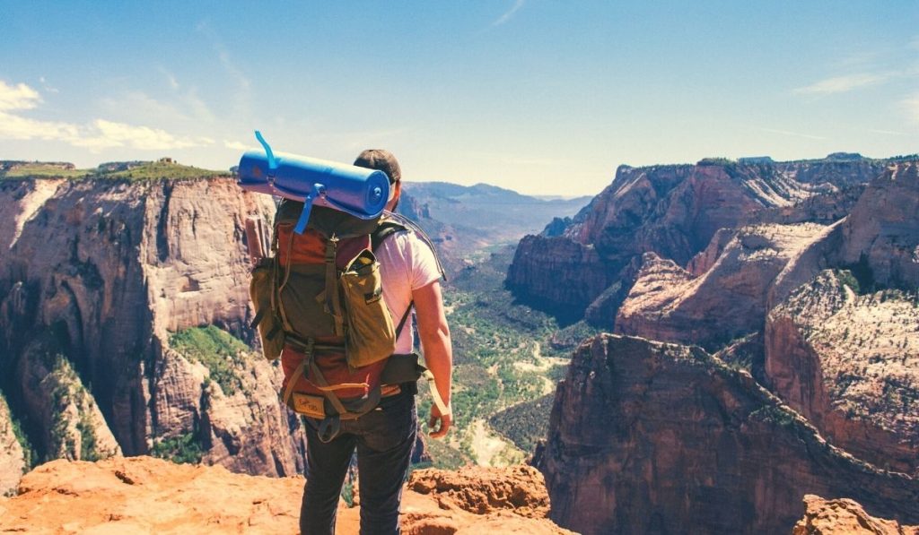 man with a backpack standing on top of a cliff in zion national park