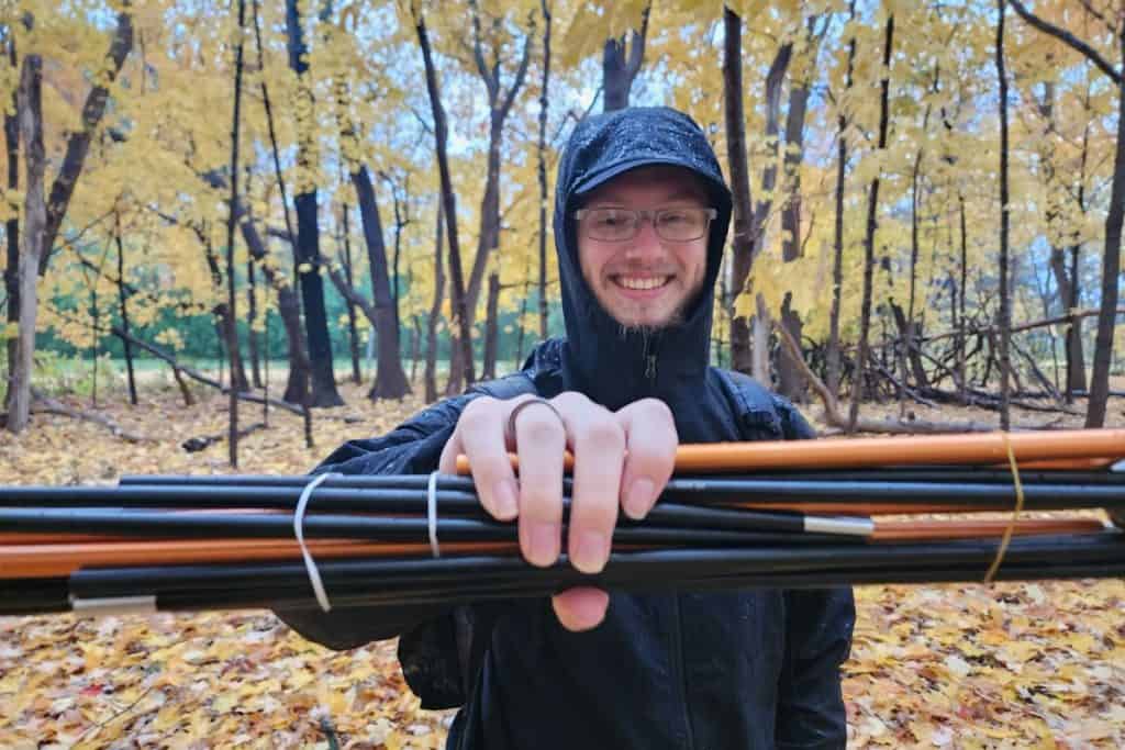 man in black jacket holding orange and black poles in the forest
