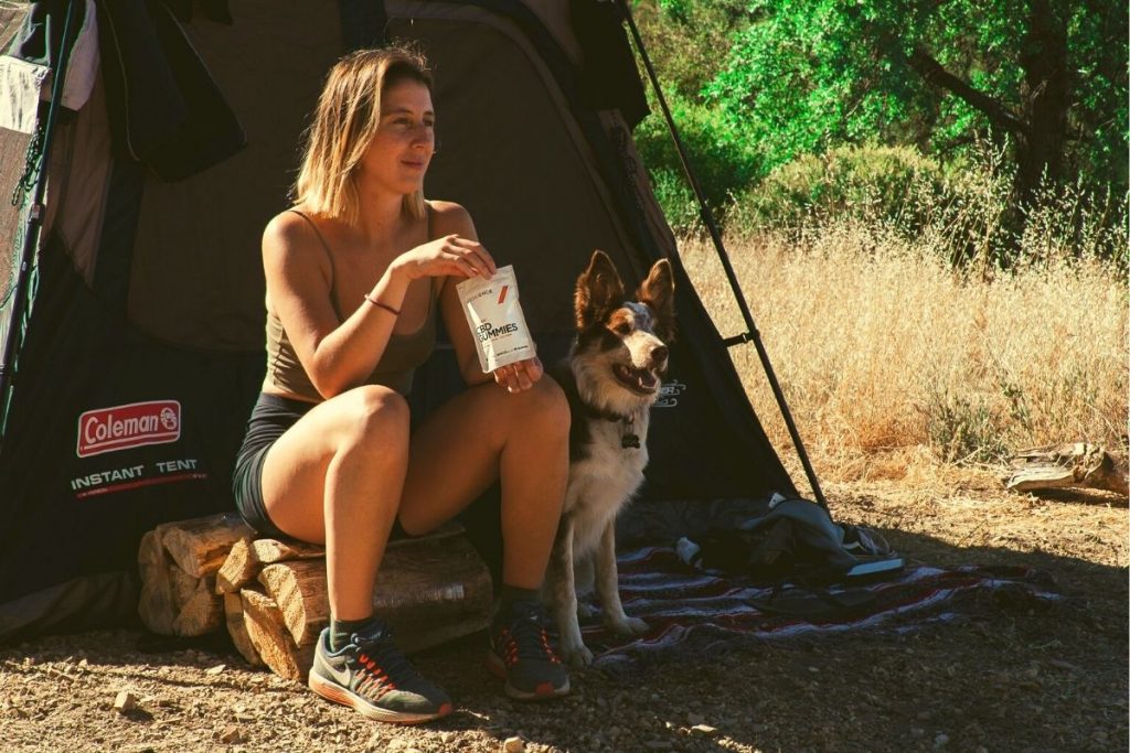 woman sitting on logs next to a dog and tent while eating