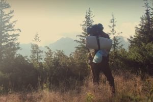man standing near a forest with a backpack