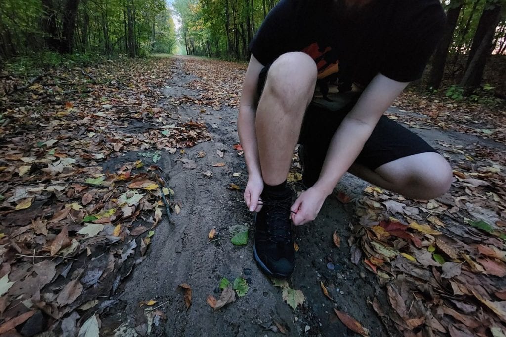 man squatting to tie his black boots on a trail