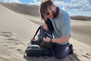 man in sunglasses packing a backpack in sand
