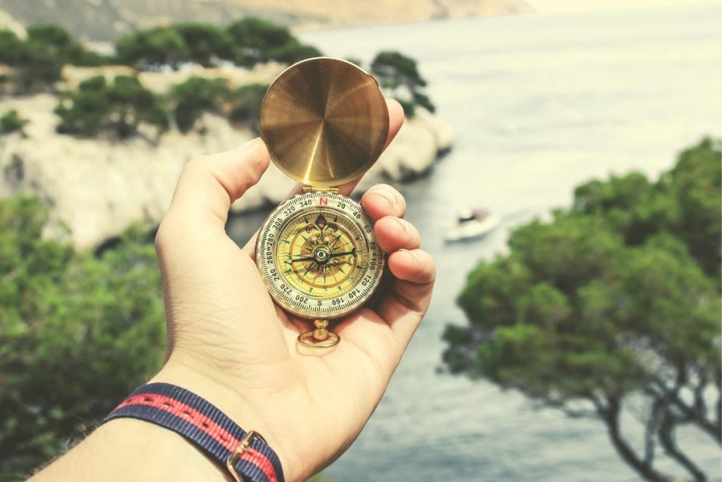 man holding a gold compass in his hand in front of water and trees