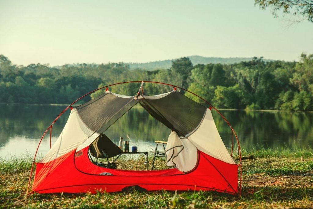 red white and gray tent pitched next to a lake with trees