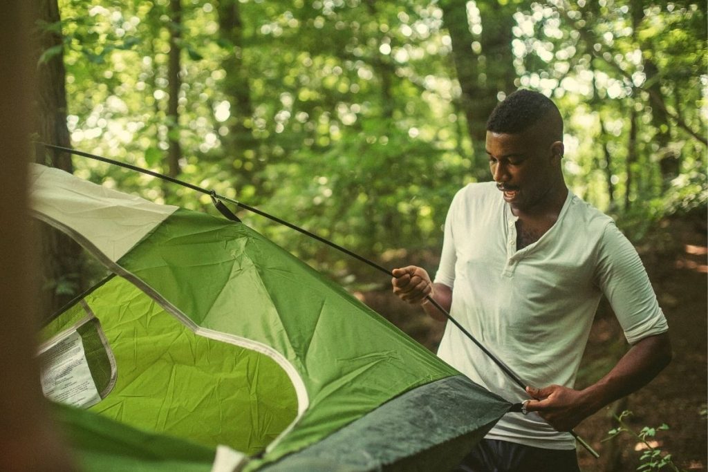 man holding the poles of a green tent in the forest