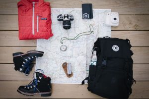shoes, a red vest, a camera, and a backpack on a white sheet